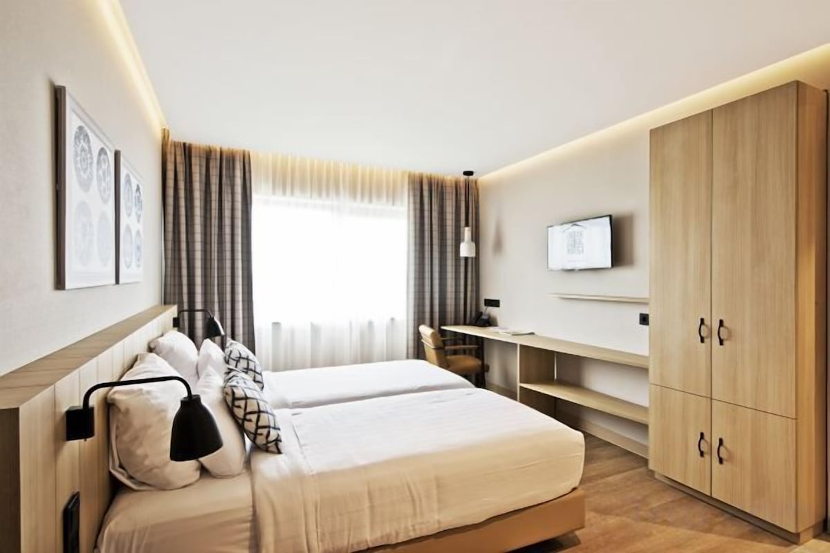 A hotel room with a bed, bedside tables, a desk, a wardrobe, and a television.