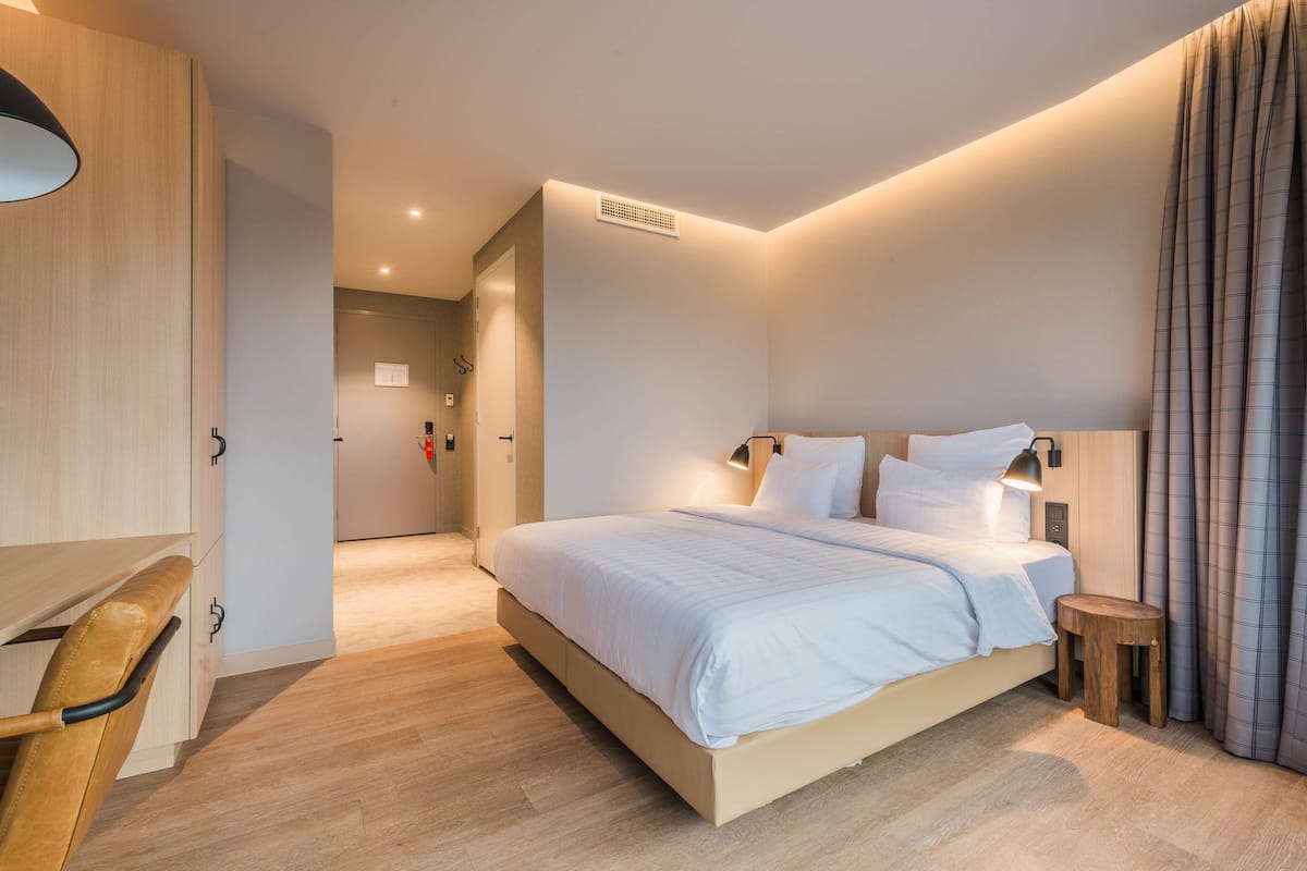 A modern hotel room with a large bed, a desk, and a chair.