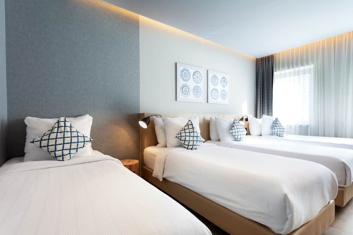 A hotel room with two beds, a bedside table, a wall-mounted lamp, and a window with curtains.