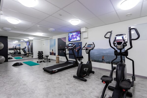 Un gimnasio con cintas de correr, elípticas y pesas libres.