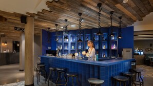 A bar area with a blue tiled bar counter, hanging pendant lights, and stools. - Urban Lodge Hotel (Amsterdam)
