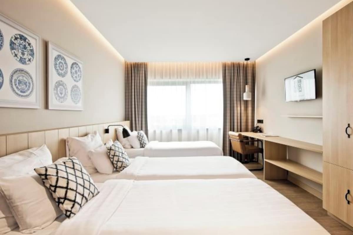 A hotel room with two beds, a desk, a chair, a TV, and artwork on the walls.
