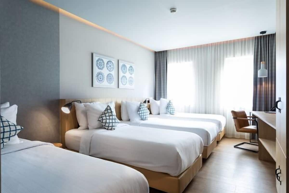 A hotel room with three beds, a desk, and a chair. There are curtains and a ceiling light.