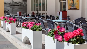 Outdoor seating with white planters of pink flowers, tables, and chairs.