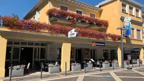 A hotel with a yellow facade, outdoor seating, and flower boxes.