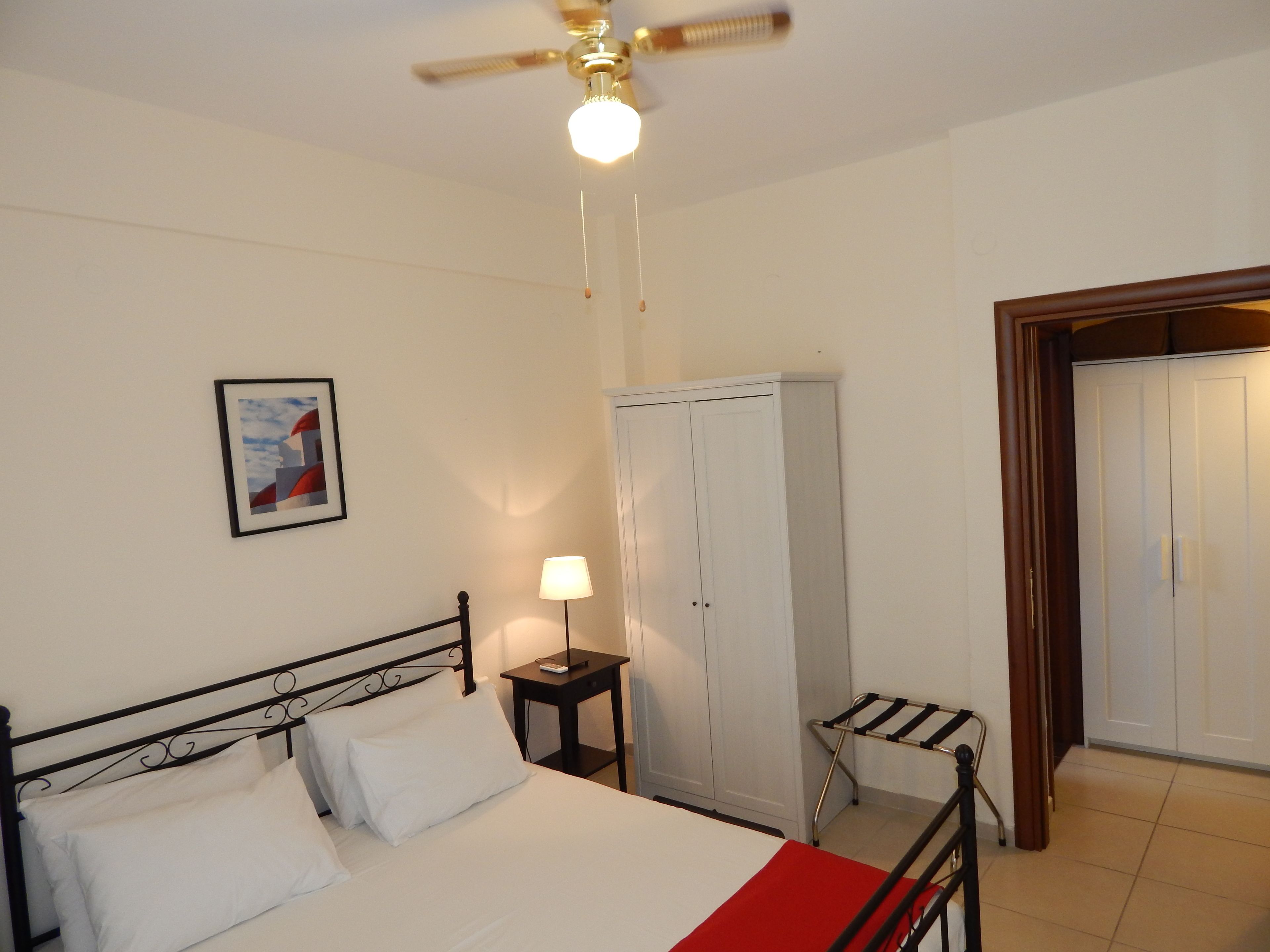 Un dormitorio con cama, lámpara de noche, armario y ventilador de techo.