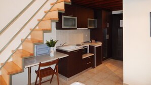 A modern kitchen with a wooden staircase, stainless steel appliances, and a small dining area. - Kripis Studio Pefkohori (Kassandra)