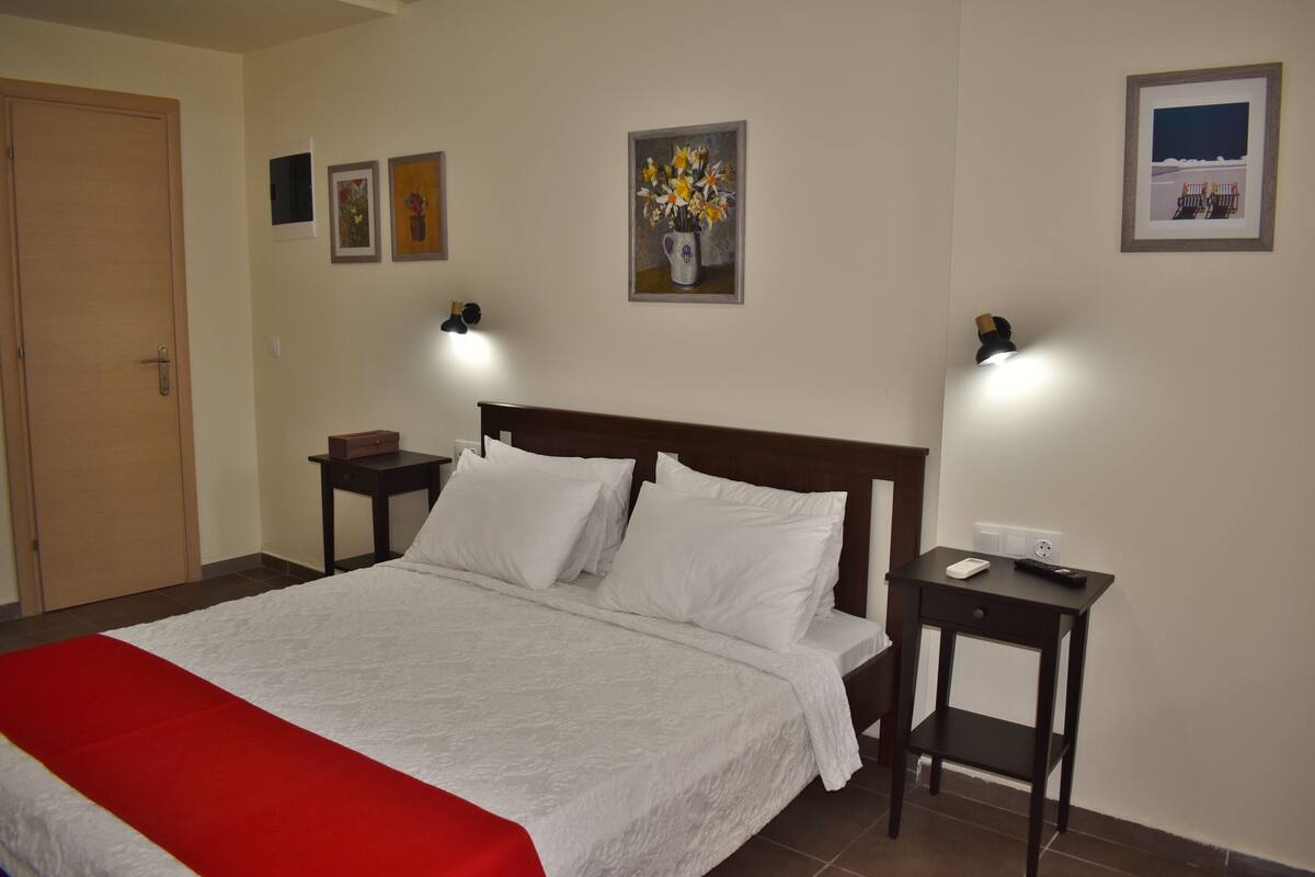 A neatly made bed with white linens and a red accent, two bedside tables with lamps, and a door to the left.