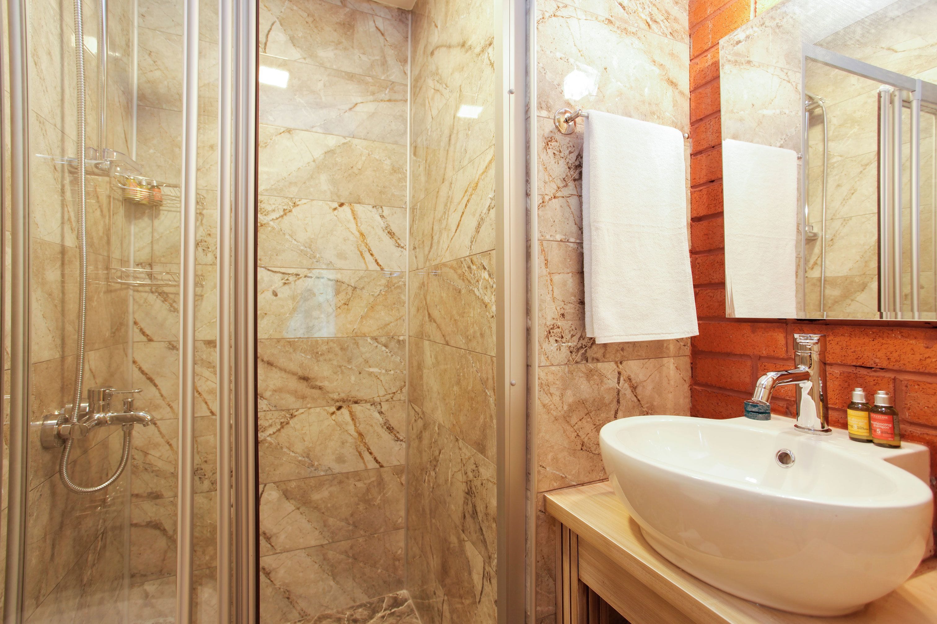 Un bagno con doccia vetrata, parete rivestita in marmo, lavabo con specchio e mobile vanitario in legno.