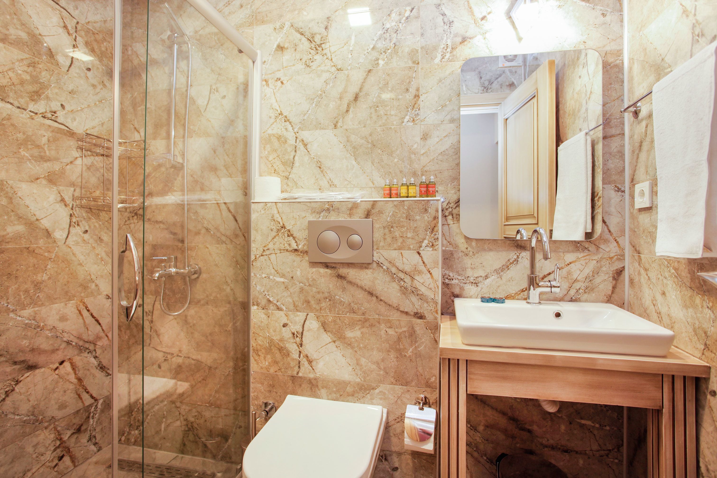 A bathroom with a glass shower enclosure, a white sink, and a marble-tiled wall.