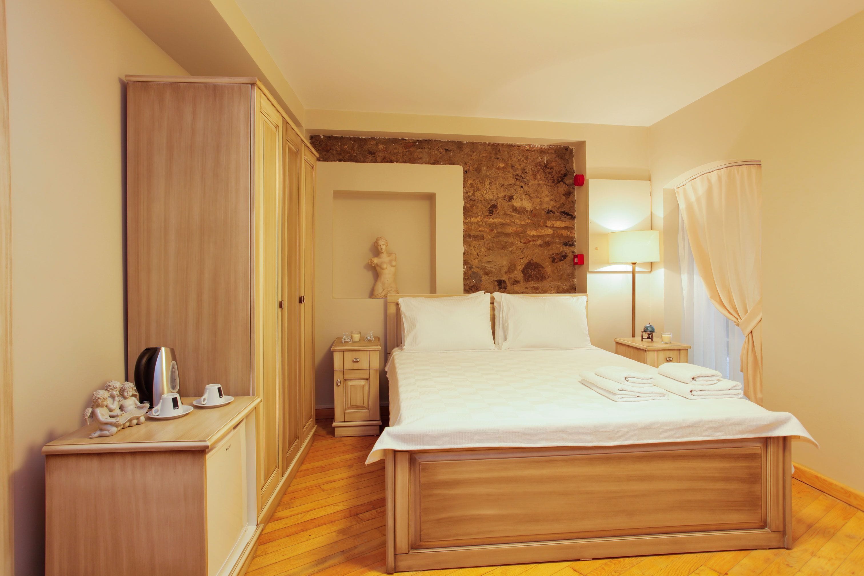 Une chambre d’hôtel avec un lit en bois, une table de chevet, une commode, une armoire et un mur en pierre.