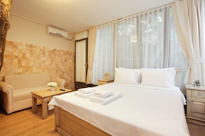 A hotel room with a bed, a sofa, a small table with a vase of flowers, and a nightstand.