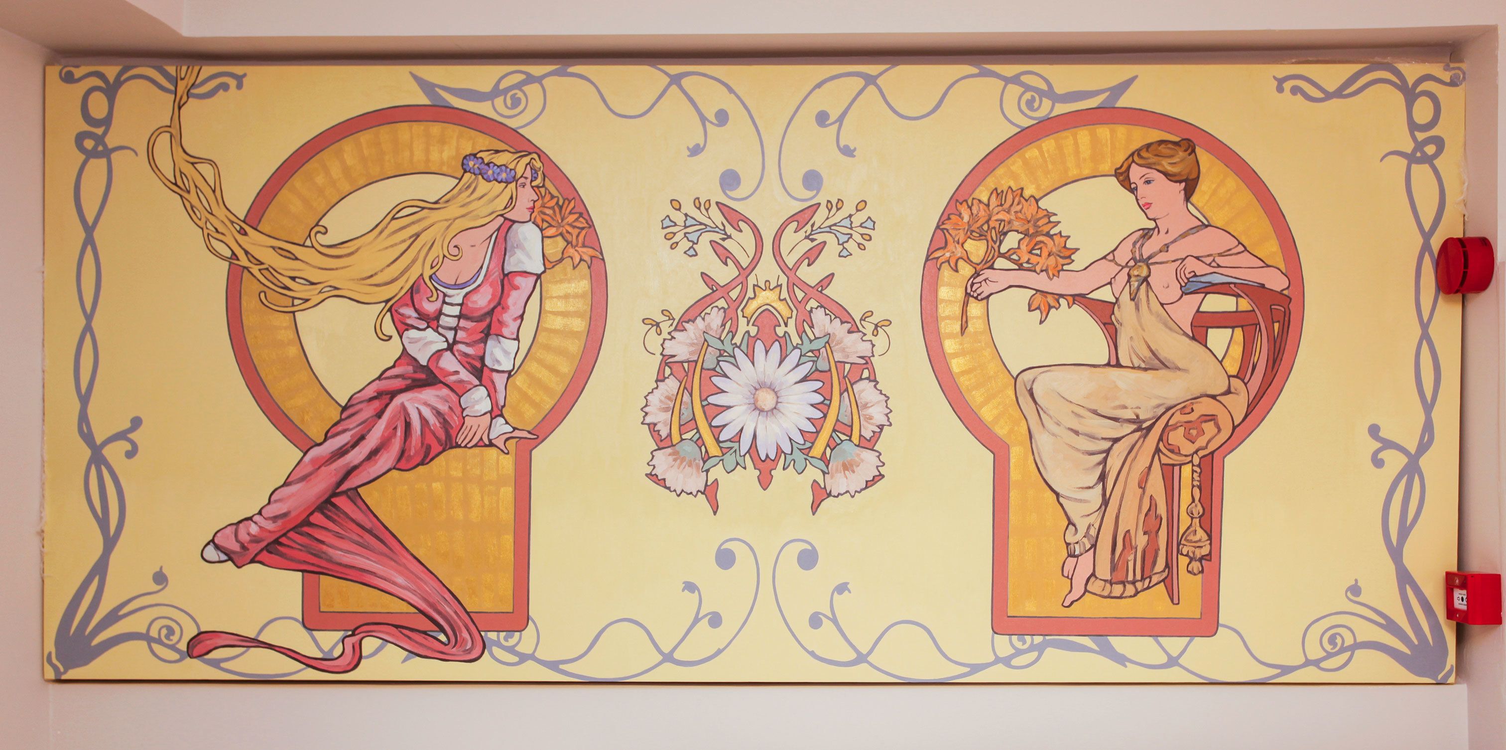 Eine Wand mit zwei kreisförmigen Mustern, die Frauen in weiten Kleidern zeigen, umgeben von floralen Elementen und dekorativen Spiralen.