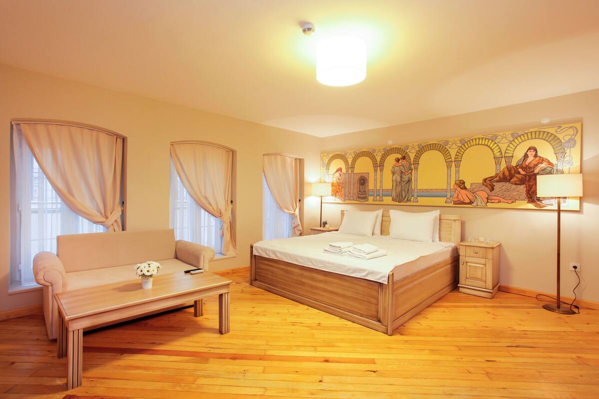 A hotel room with a large bed, a sofa, a small table, and a nightstand.