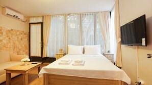 A hotel room with a bed, a small table with a vase of flowers, a nightstand, a TV mounted on the wall, and a window with curtains. - The Loft Istanbul (Istanbul)