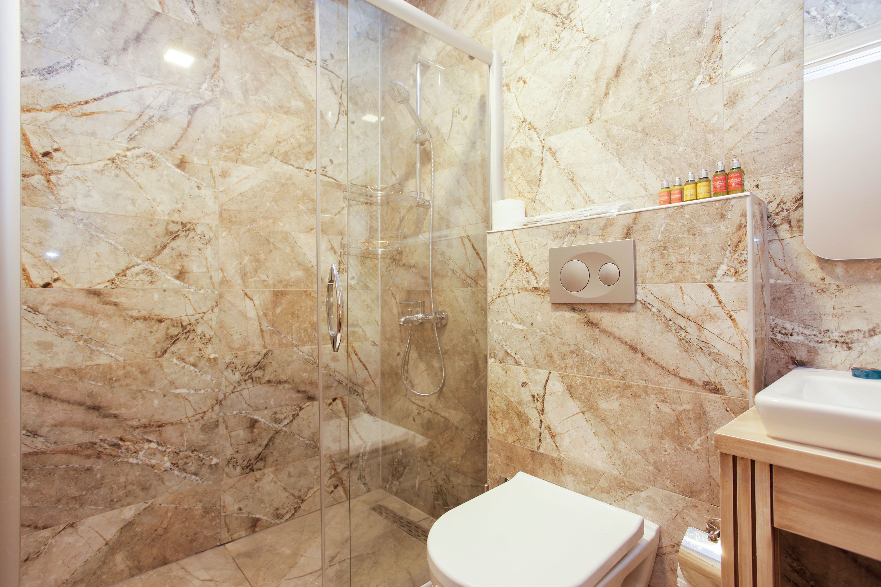 A bathroom with a glass-enclosed shower, a white toilet, and a marble wall.