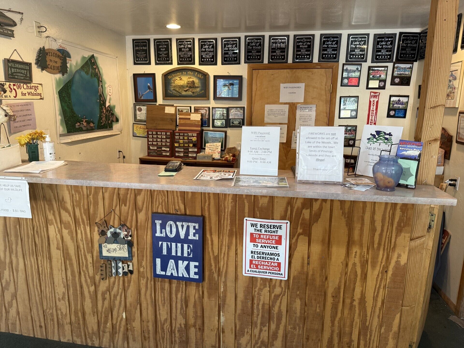 A reception desk with various signs, including a 'Welcome to the Lake' sign, a 'Love the Lake' sign, and multiple 'Best Cabin Retreat' signs.