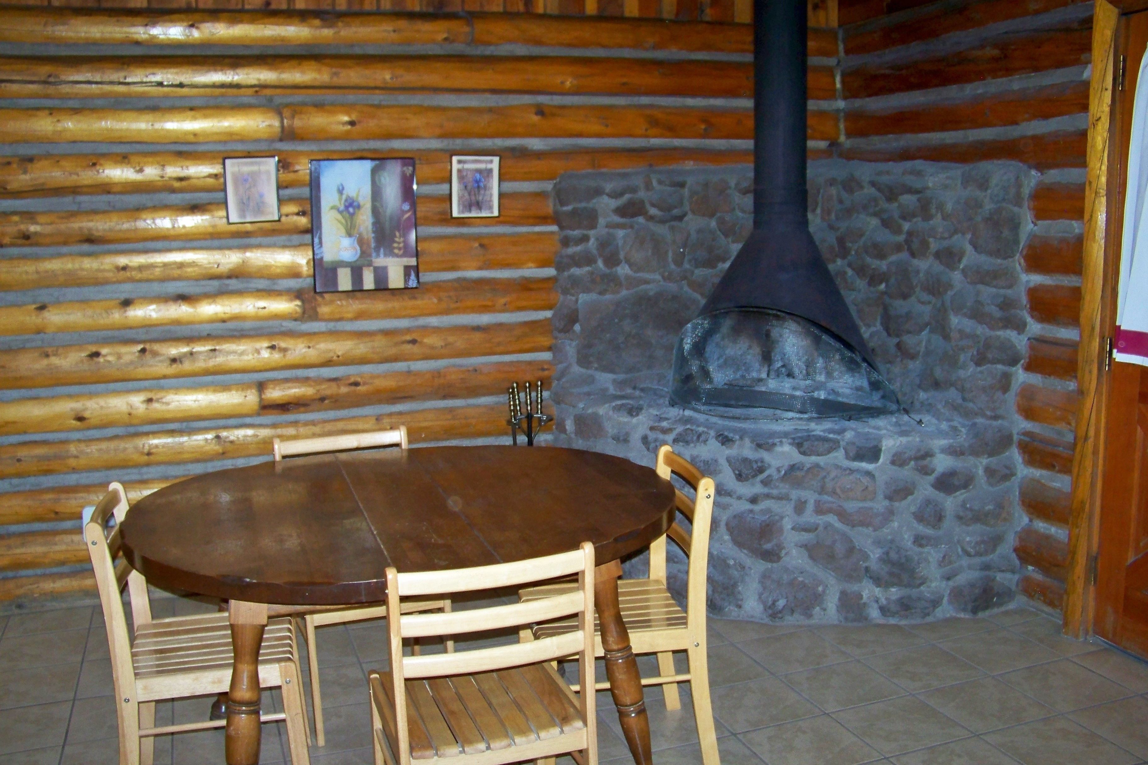 L’intérieur d’un chalet en rondins de bois, avec une cheminée en pierre, une table à manger en bois et des chaises.