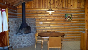 A log cabin interior with a stone fireplace, wooden walls, a round wooden table, and two wooden chairs. - Lake of the Woods Resort (Lakeside)