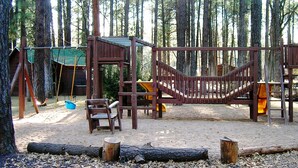 A playground with wooden structures, swings, and a slide, surrounded by trees. - Lake of the Woods Resort (Lakeside)