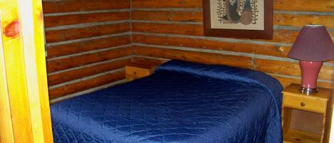 A wooden cabin room with a bed, a nightstand, and a framed picture on the wall.
