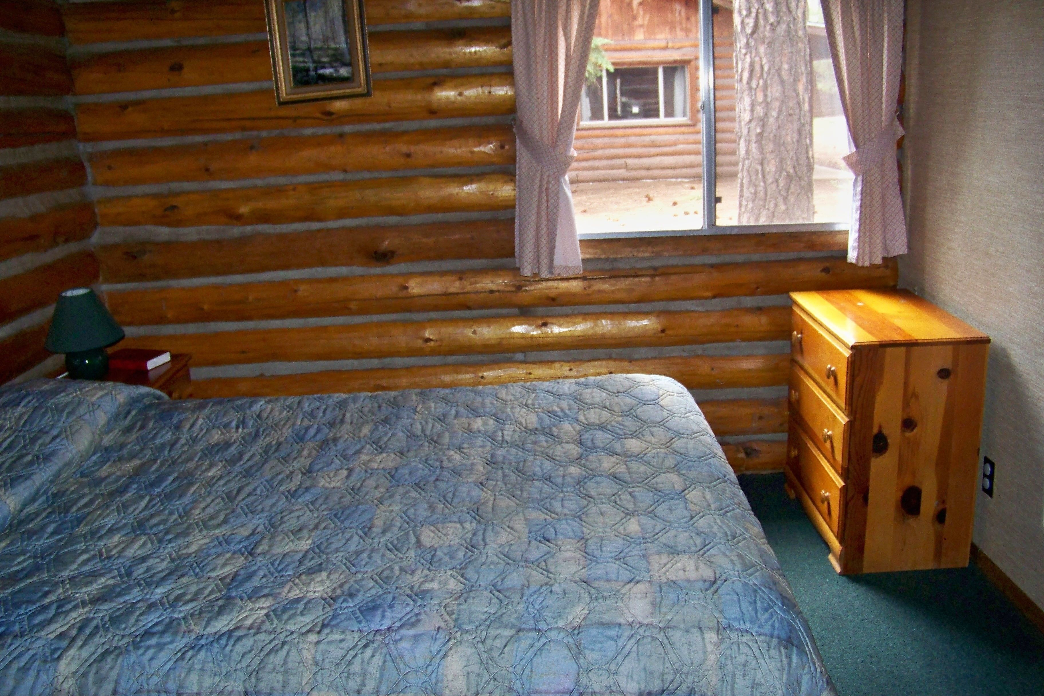 Una habitación tipo cabaña de madera con cama, cómoda y ventana con cortinas.