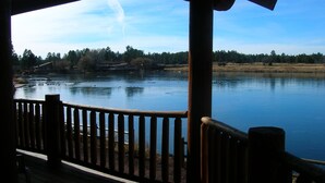 A wooden deck with a railing overlooking a calm lake, surrounded by trees and a clear sky. - Lake of the Woods Resort (Lakeside)