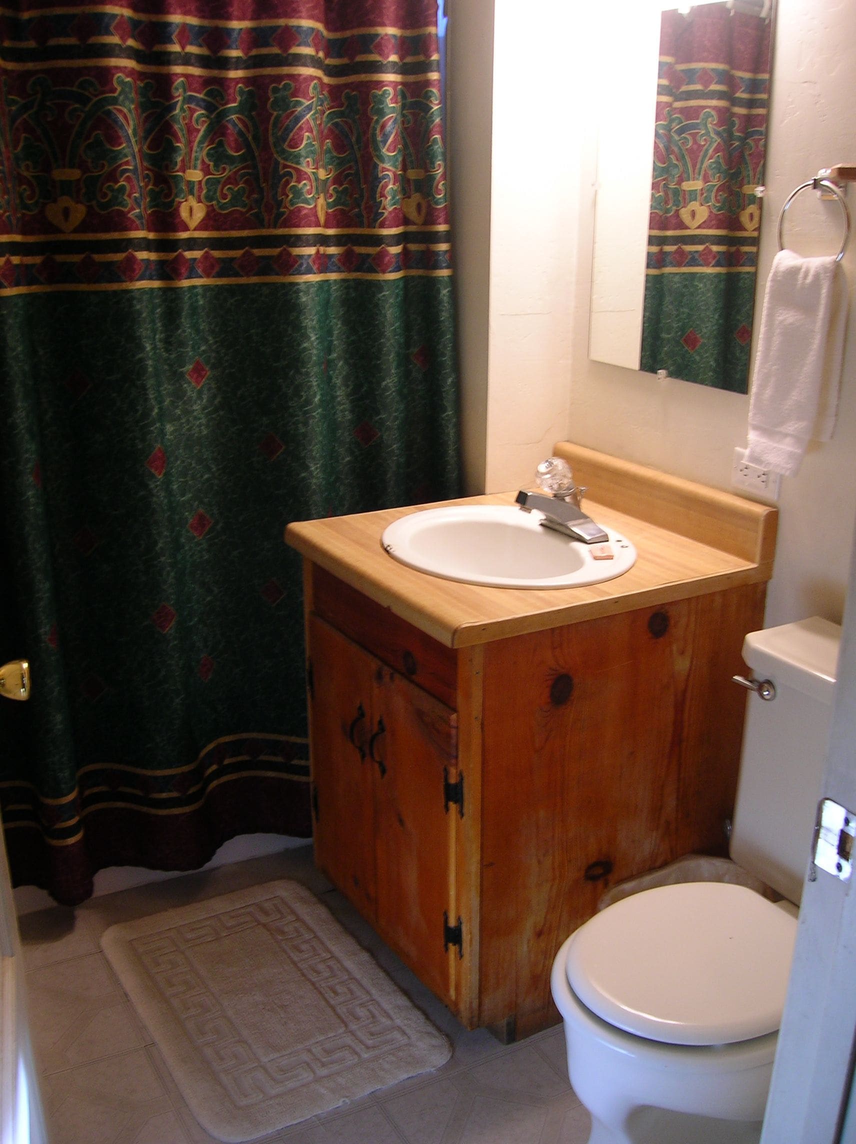 A bathroom with a wooden vanity, a white sink, a toilet, and a shower curtain with a patterned design.