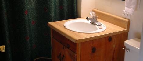 A bathroom with a wooden vanity, a white sink, a toilet, and a shower curtain with a patterned design.