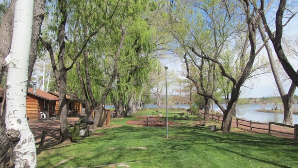 A park with picnic tables, a wooden cabin, and a lake. - Lazy Oaks Resort (Lakeside)