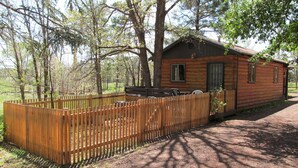 A rustic wooden cabin with a fenced yard, surrounded by trees. - Lazy Oaks Resort (Lakeside)