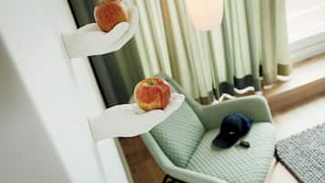 Een kamer met een groene fauteuil, een wit wandplankje met twee appels, en een raam met gordijnen.