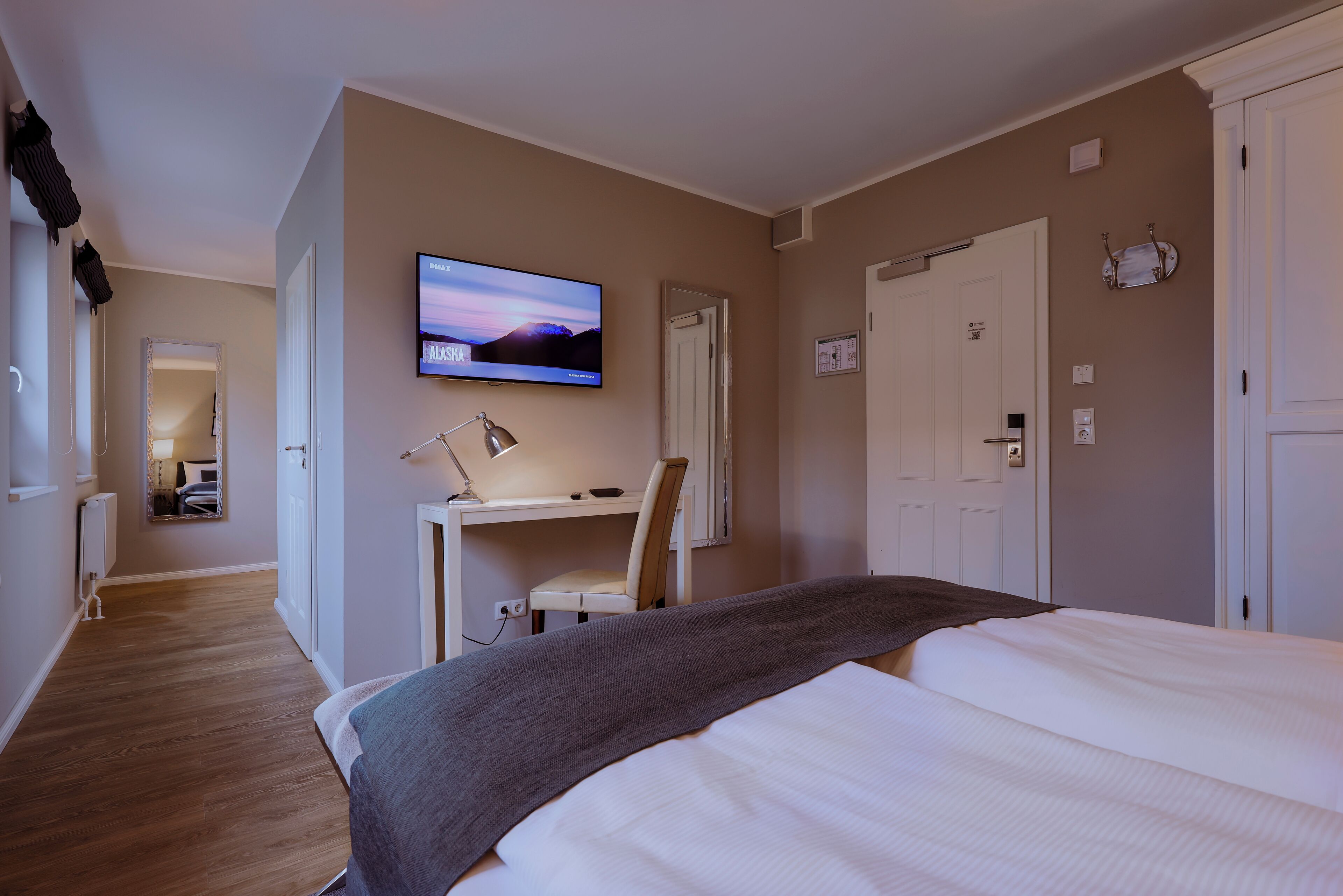 Habitación de hotel con cama, escritorio, silla, televisión y puerta.