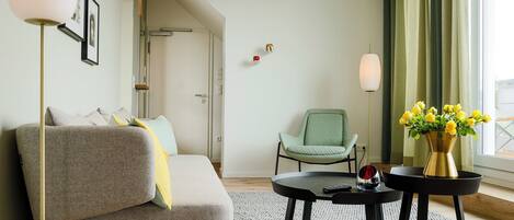Una sala de estar moderna con un sofá gris, un sillón verde, una mesa redonda negra con un florero de flores amarillas y una lámpara de pie.