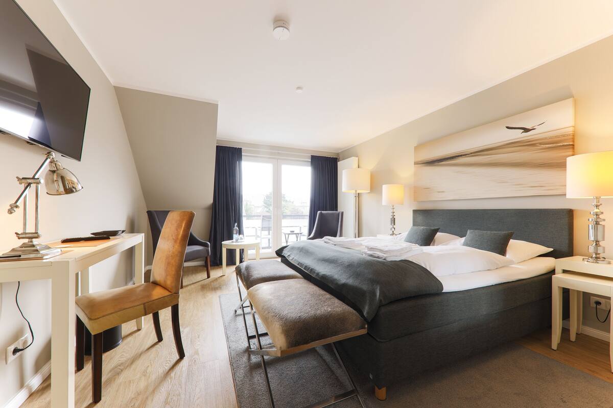 A hotel room with a bed, desk, chair, and a large window.