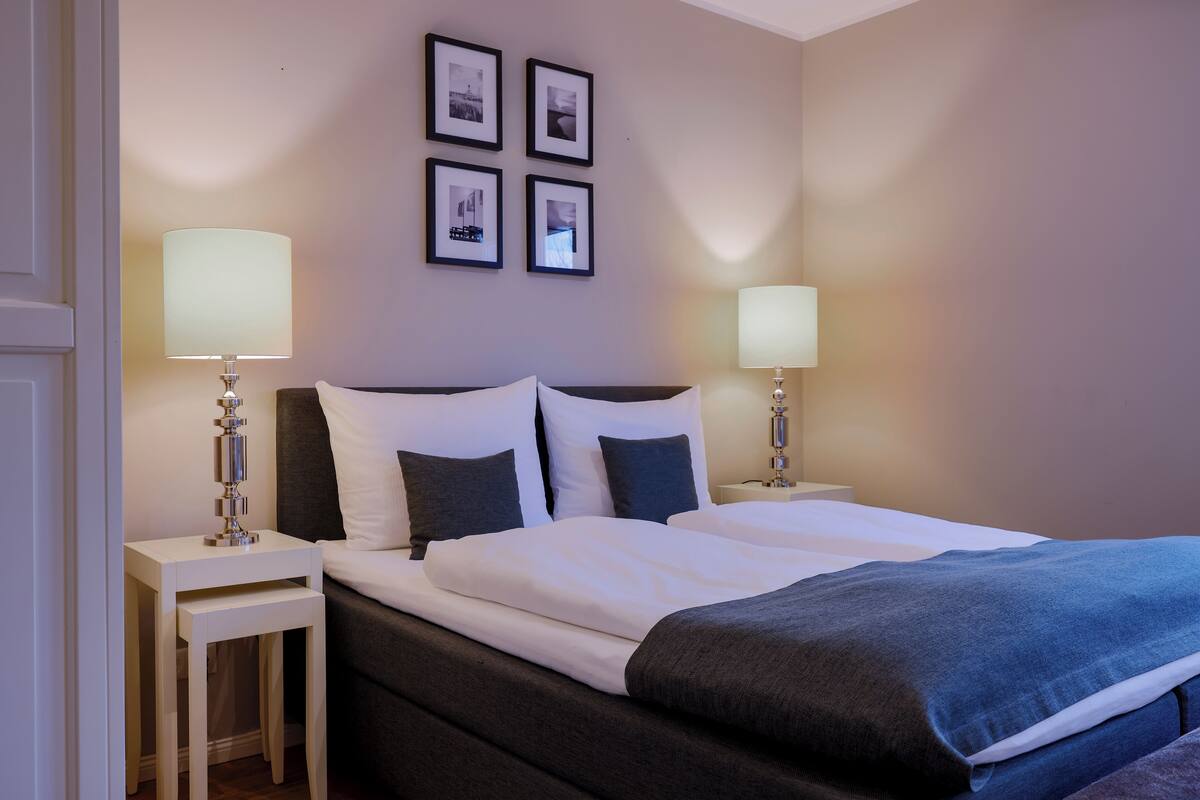 A hotel room with a bed, two bedside tables, and four framed pictures on the wall.