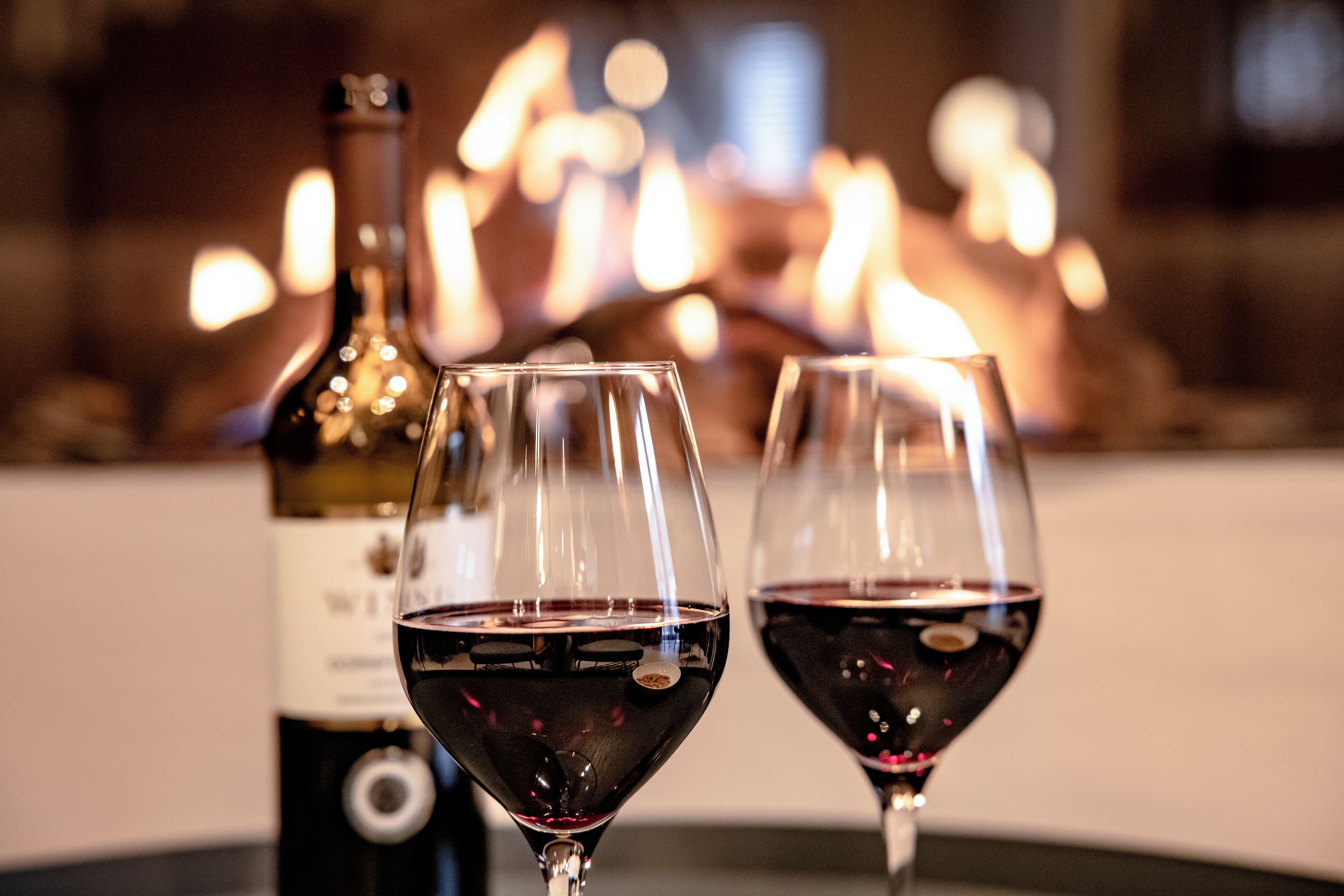 Zwei Weingläser mit Rotwein und eine Weinflasche im Hintergrund.