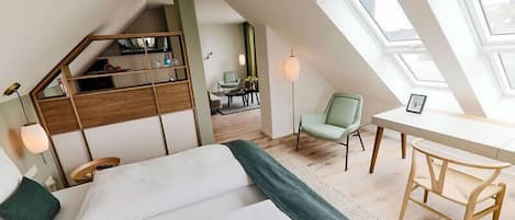 Un dormitorio tipo loft moderno con una cama grande, un escritorio y una silla. Se ve una escalera que sube a un nivel superior con una estantería.