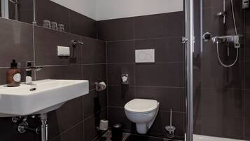 Ein modernes Badezimmer mit einer Duschkabine, einem weißen Waschbecken und einer Toilette.