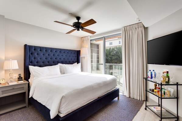 A hotel room with a large bed, a ceiling fan, a TV, a nightstand with a lamp, and a view of the outdoors through a sliding door.