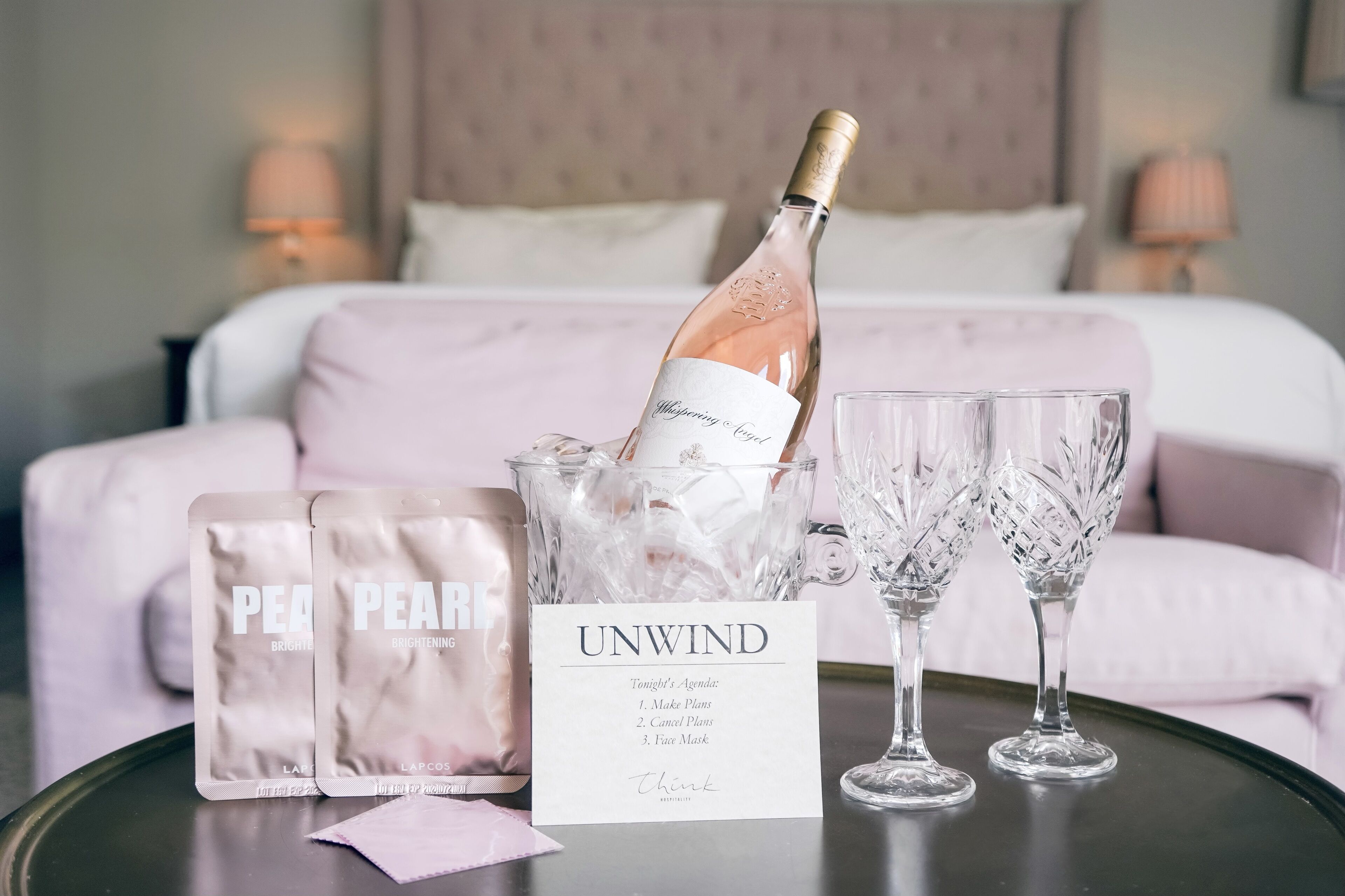 A bottle of champagne in a glass container with two glasses beside it, a tissue, and a card with a list of tasks.