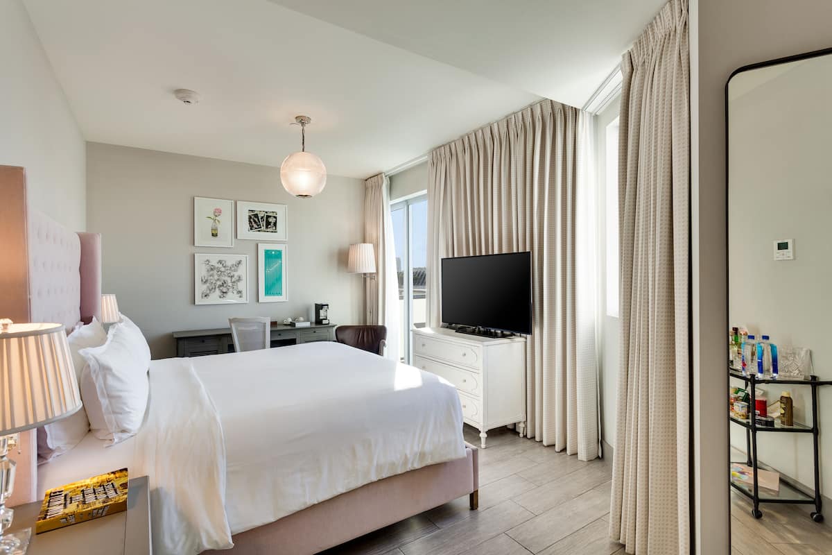 A modern hotel room with a large bed, a flat-screen TV, a desk with a lamp, and a bookshelf.