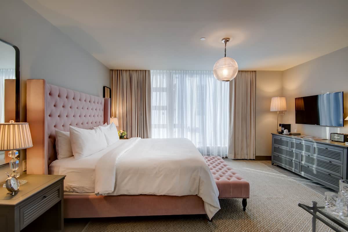 A spacious hotel room with a large bed, a television, a dresser, and a window with curtains.