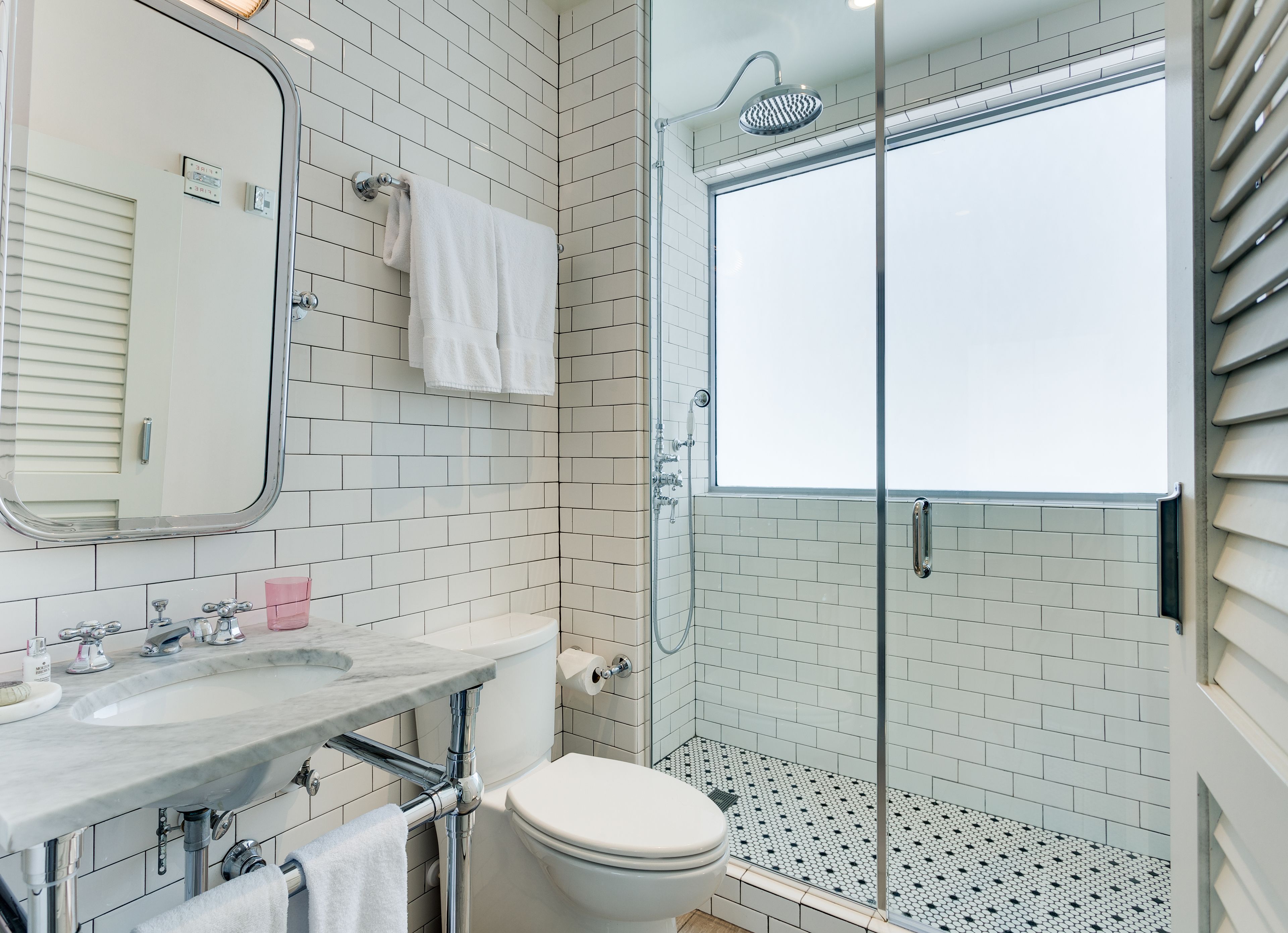 Ein modernes Badezimmer mit Duschkabine aus Glas, weißen Fliesen, einem Marmorwaschbecken und einer Toilette.
