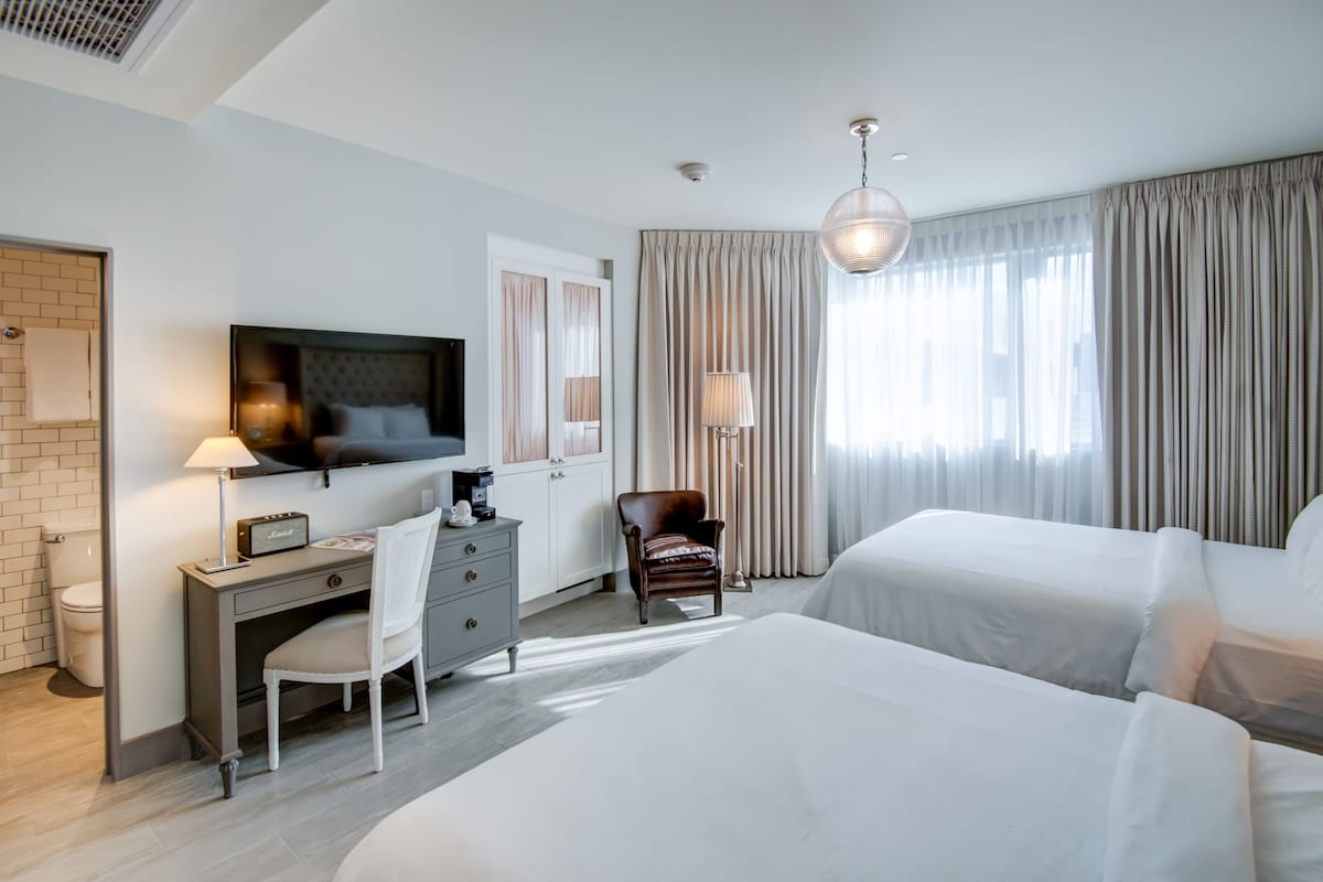 A hotel room with two beds, a desk, a chair, a TV, and a window with curtains.