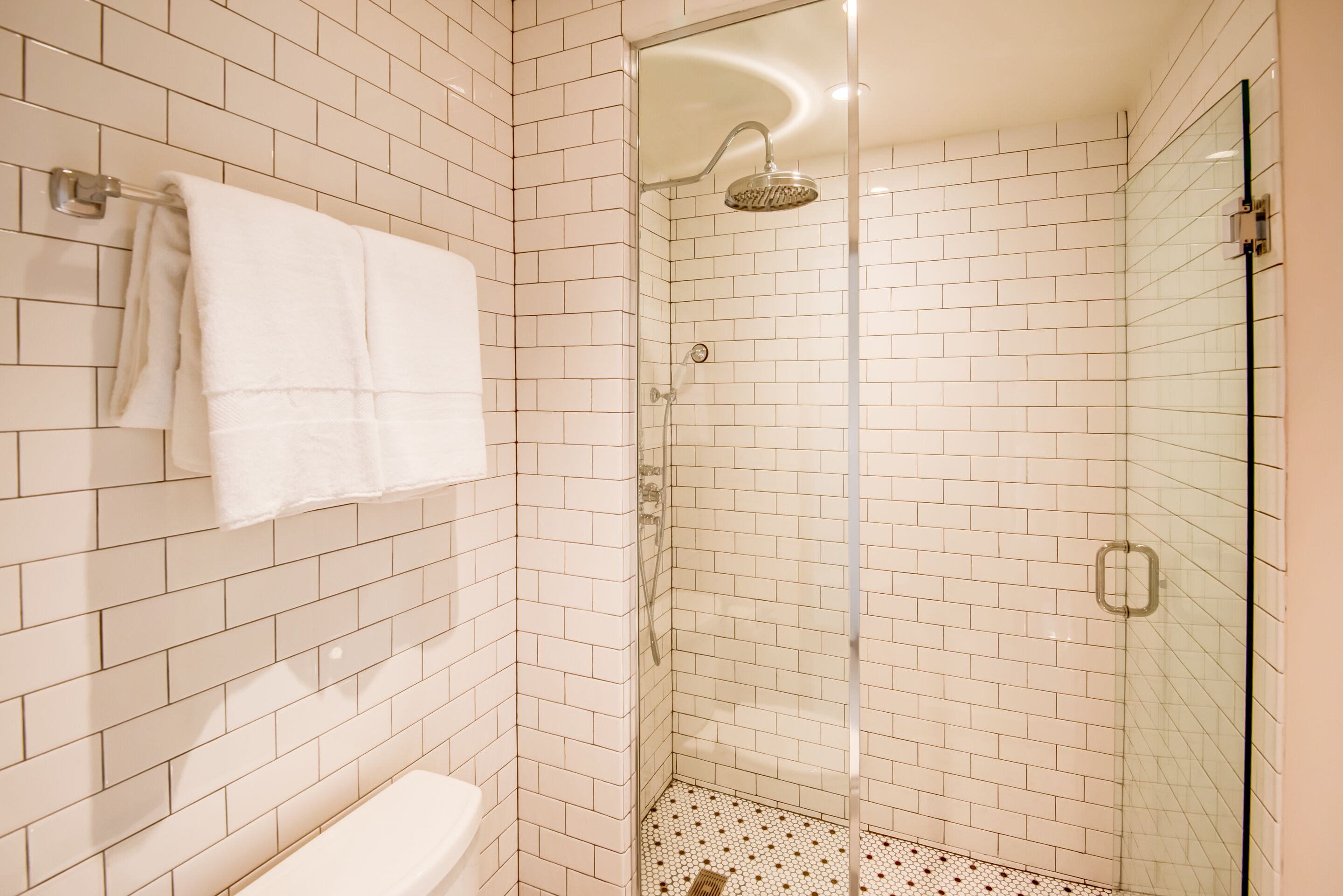 A modern bathroom with white subway tiles, a glass-enclosed shower, and a white toilet.