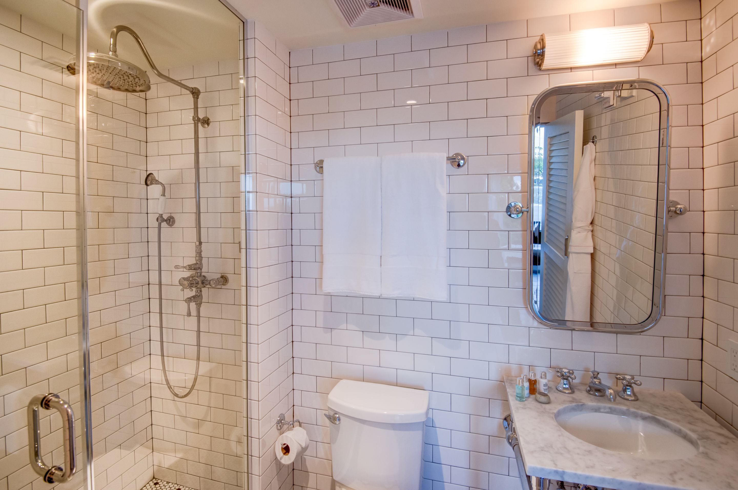 Een moderne badkamer met witte betegelde wanden, een douchecabine met glazen wanden, een toilet, een wastafel met spiegel en een handdoekhouder.