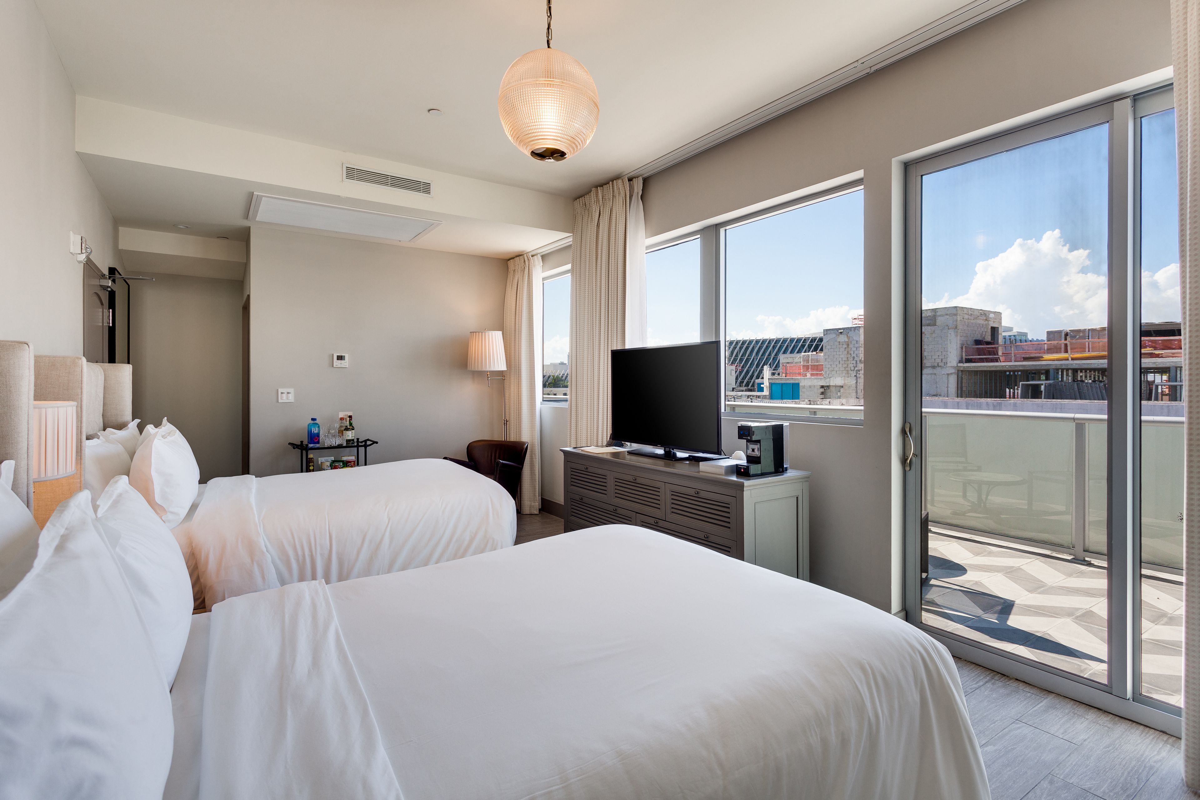 A hotel room with two beds, a television, a desk with a lamp, and a balcony with a view of the city.