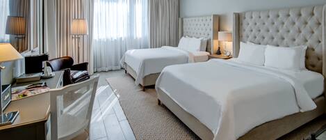 A hotel room with two beds, a desk, a chair, a lamp, and a large window with curtains.