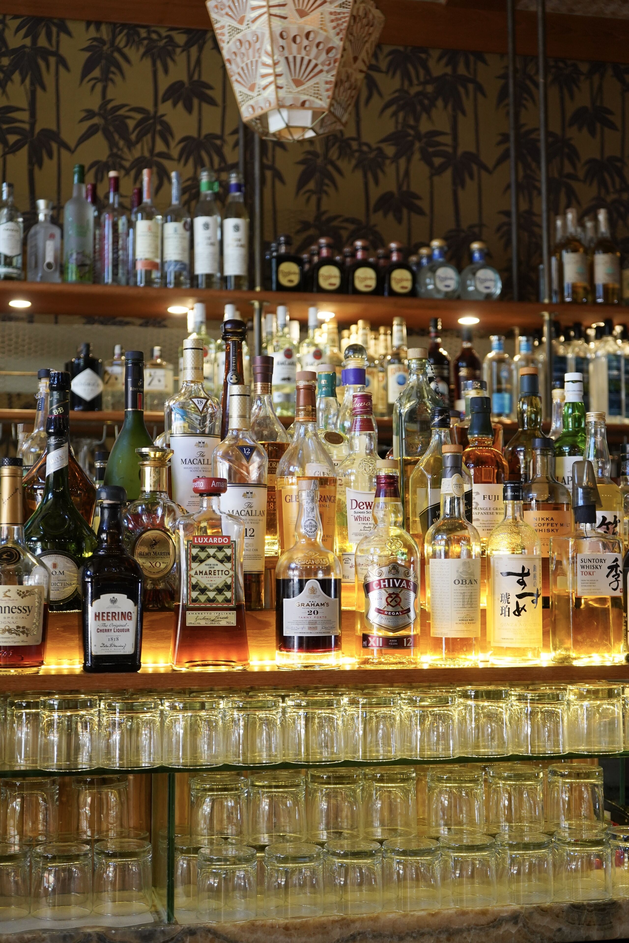 A bar area with a variety of liquor bottles and empty glasses on shelves.